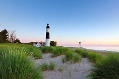 a light house sitting on top of a beach next to tall green grass and water