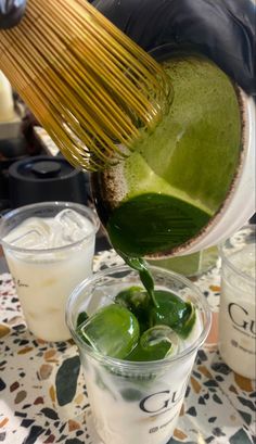 a person pouring green tea into a cup on top of a table with other drinks