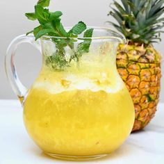 a glass pitcher filled with lemonade next to a pineapple on a white table