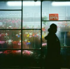 a person standing in front of a window with flowers behind it and an open sign above the window