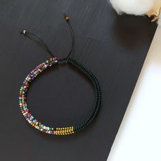 a multi - colored beaded bracelet sitting on top of a black surface next to a cotton ball