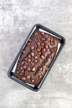 a loaf of chocolate cake in a pan on top of a cement surface with nuts