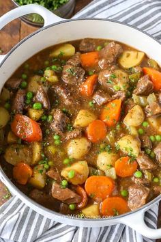 beef stew with carrots, potatoes and peas in a white pot on a striped cloth