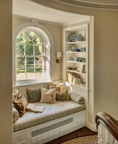 a window seat with pillows on it in front of a bookshelf