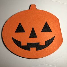 an orange pumpkin shaped cutting board with two faces carved into the front and back, sitting on a white surface