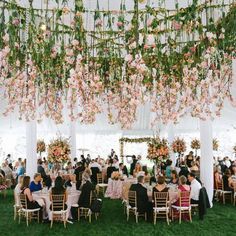 a group of people sitting at tables under a tent with flowers hanging from the ceiling