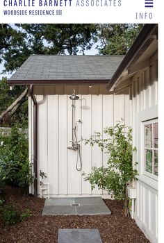 a small white shed with a shower in it's corner and plants growing outside