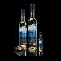 two bottles of alcohol sitting next to each other on a black surface with mountains in the background