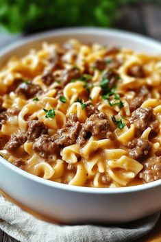 a white bowl filled with pasta and meat on top of a wooden table next to a napkin