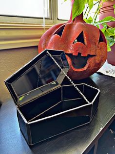 a black box with a pumpkin face on it sitting next to a potted plant