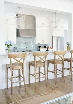 three wooden chairs sitting in front of a white kitchen island with an oven and refrigerator