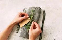 a person holding a piece of paper on top of a napkin next to a fork and knife