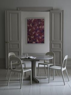 a white table and chairs in front of a painting on the wall with doors open