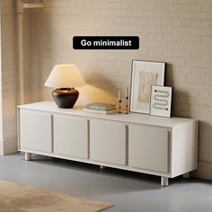 a white cabinet with a lamp and pictures on it next to a brick wall that says go minimalist