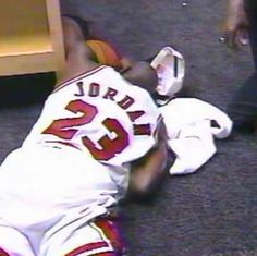 a baseball player laying on the ground with his head in his hands and another person standing next to him