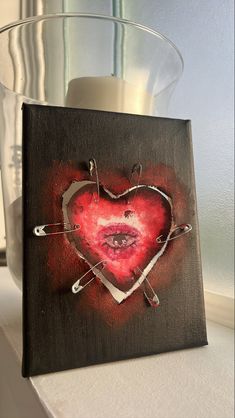 a heart shaped painting on a wooden block next to a candle