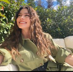 a woman sitting on top of a white couch in front of trees and bushes smiling at the camera