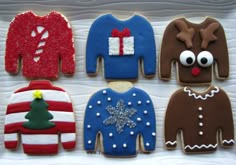 four decorated cookies in the shape of sweaters and reindeer's noses are on a plate