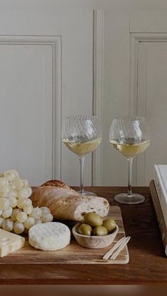 two glasses of wine, cheese and bread on a wooden table next to an open book