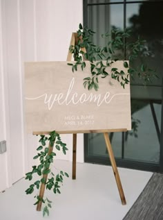 a welcome sign sitting on top of a wooden easel next to a door with greenery