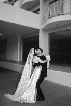 a bride and groom embracing in front of an apartment building with balconies on the second floor