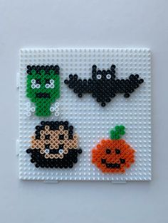 three halloween bead art pieces on a white surface with pumpkins and bats in the background