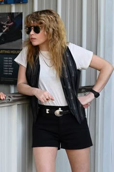 a woman leaning against a wall with her hands on her hips and wearing black shorts