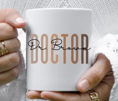 a woman is holding a coffee mug with the word doctor on it in gold lettering