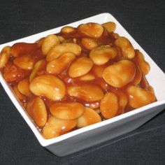 a square white bowl filled with peanuts covered in caramel sauce on a black surface