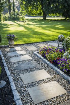 a garden with flowers and stones in the middle, along side a path that leads to a grassy area