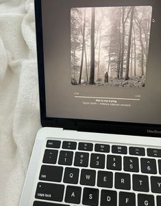 an open laptop computer sitting on top of a white bed next to a forest filled with trees