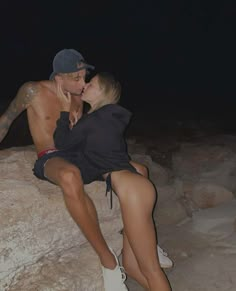 a man and woman sitting on top of a large rock in the desert at night