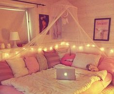 a laptop computer sitting on top of a bed covered in pink and white pillows with lights