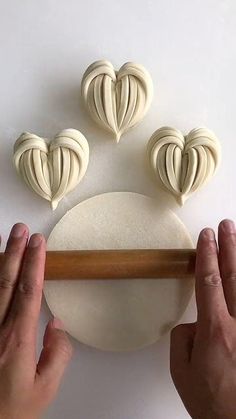 two hands are holding a rolling pin and making heart shaped doughs on a white surface