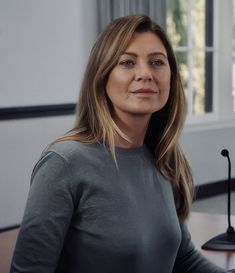 a woman sitting at a desk with a microphone in front of her and looking into the distance