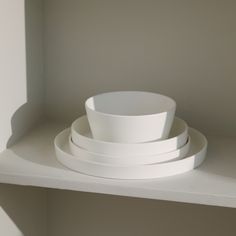 three white bowls sitting on top of a shelf