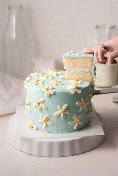 someone is cutting into a cake with blue frosting and white flowers on the side