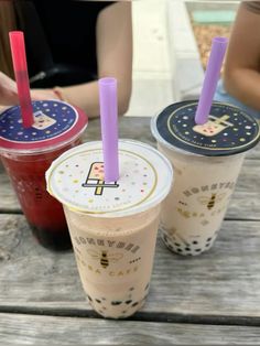 three drinks sitting on top of a wooden table next to each other with purple straws