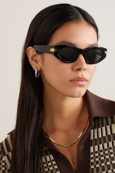 Bottega Veneta's sunglasses have classic cat-eye frames reminiscent of styles from the '60s. They're made from glossy black acetate with gray tinted lenses and polished gold-tone bars at the temples. Store yours in the case when you're not wearing them. Black Gold Sunglasses, Black Cat Eyes, Classic Sunglasses, Trending Sunglasses, Cool Sunglasses, Cat Eye Frames, Eyewear Womens, Gold Sunglasses, Black Sunglasses