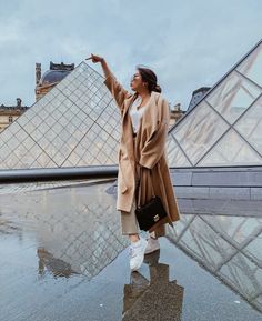 a woman standing in front of a pyramid pointing at the sky with her hand up