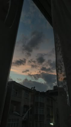 the sky is dark and cloudy as seen from an open window with curtains on it