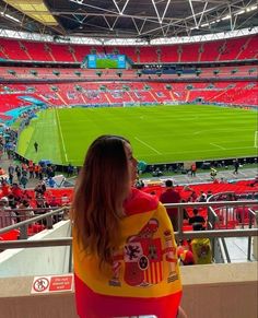 a woman is sitting in the stands at a soccer stadium looking out over the field