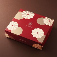 a red box with white flowers on it sitting on a brown surface next to a black background