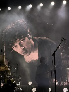 a man standing in front of a microphone on top of a stage with lights behind him