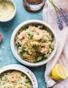 two bowls filled with rice and shrimp next to lemon wedges on a blue surface