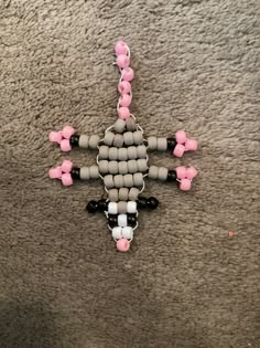 a cross made out of beads is laying on the floor with pink and black beads