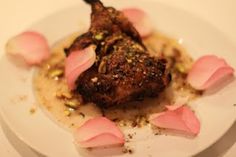 a white plate topped with meat covered in sauce and garnished with pink flowers