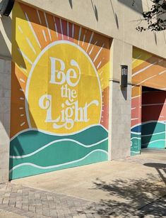 a large mural on the side of a building that says be the light with sun above it