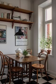 a dining room table and chairs with bookshelves above it, in front of a window