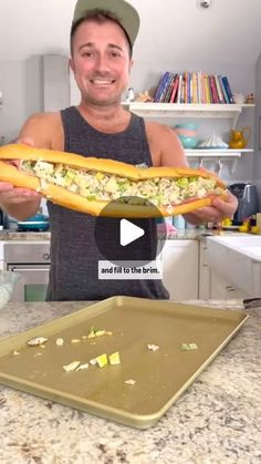 a man is holding a large sandwich in his hands and smiling at the camera while standing next to a baking sheet